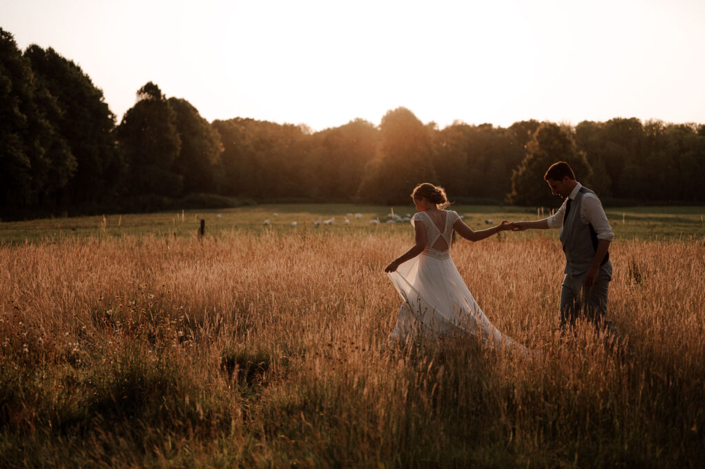 Wedding couple walking through a field during golden hour, with a dark forest in the background