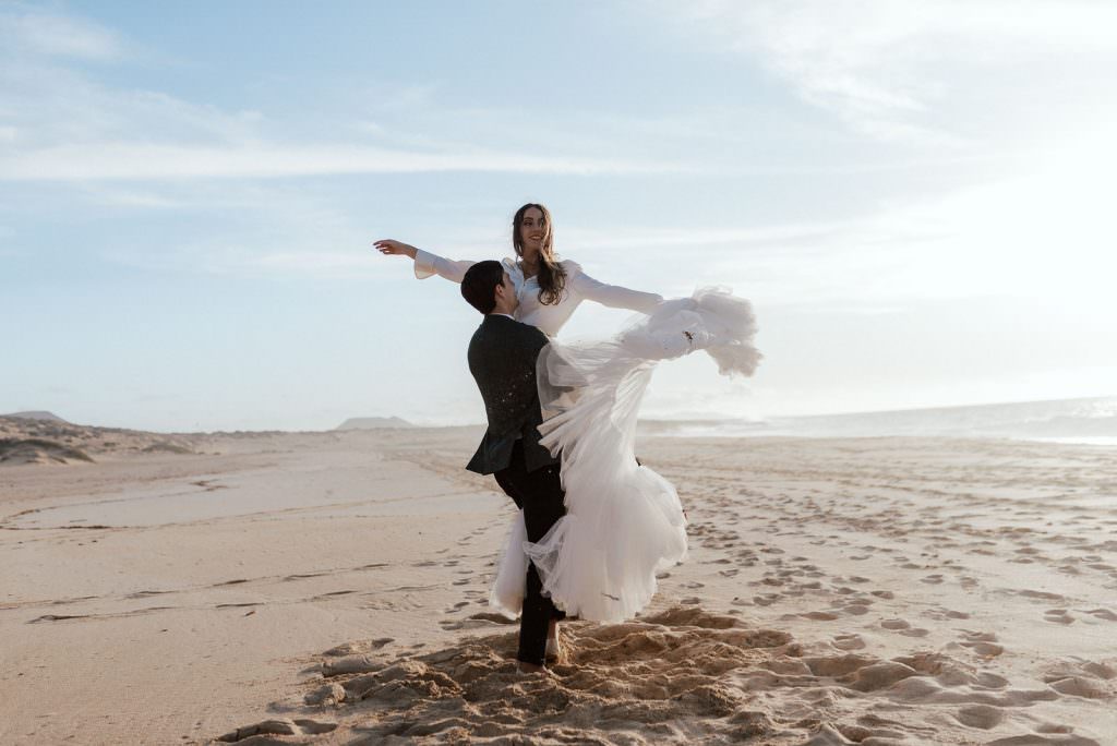 groom lifting bride on sandy beach with ocean in background during elopement in Spain