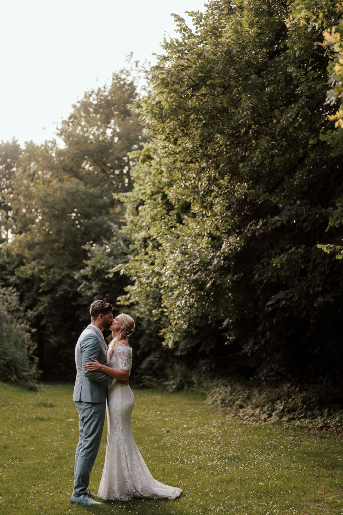 Bride and groom kissing in a green field surrounding by trees in an outdoor wedding venue in the Netherlands