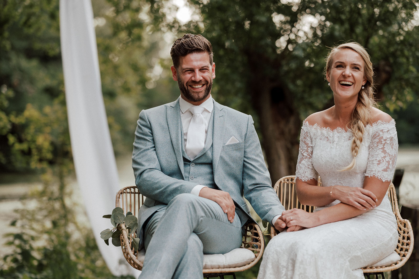 Couple sitting together during their wedding ceremony, holding hands and laughing