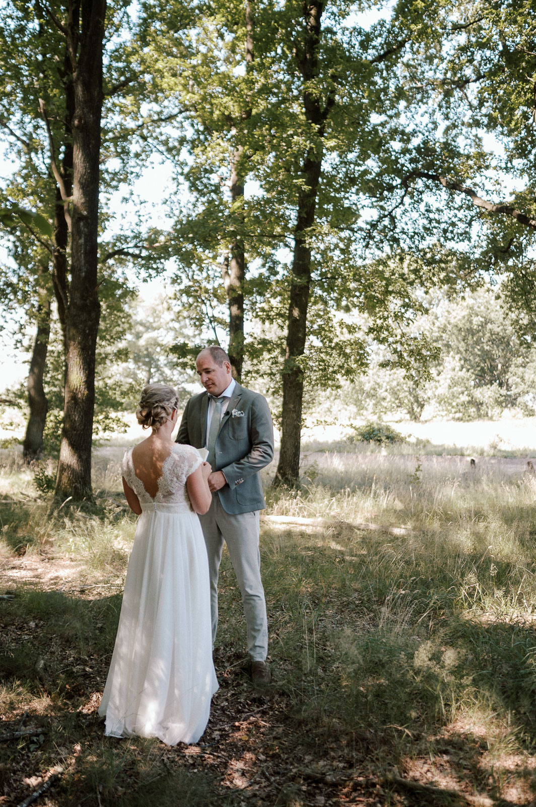 Wedding couple standing together in a forest, the bride reading her vows to the groom