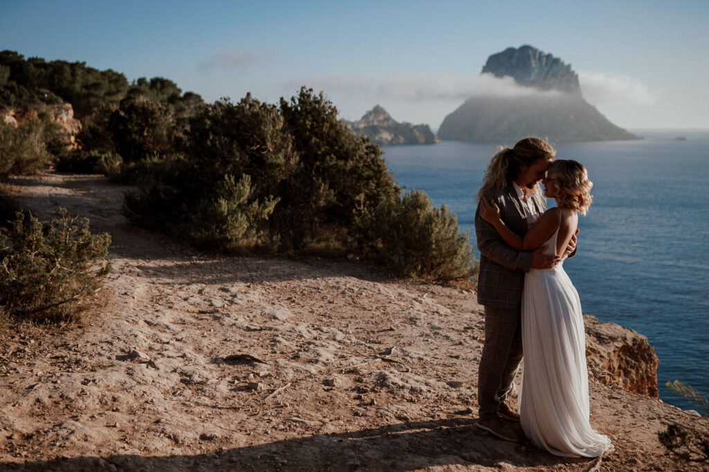 Wedding couple standing on a cliff in Spain, holding each other with the blue sea in the background