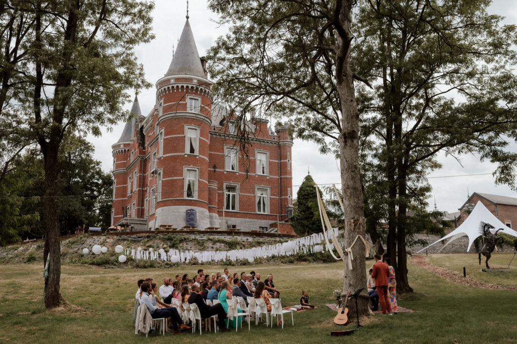 Wedding party seated together in front of Chateau de Goyet, a majestic castle in Belgium