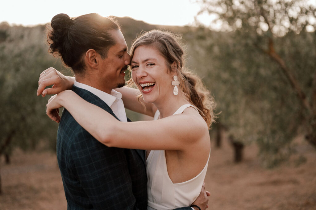 Wedding couple holding each other in an olive grove, the bride smiling into the camera