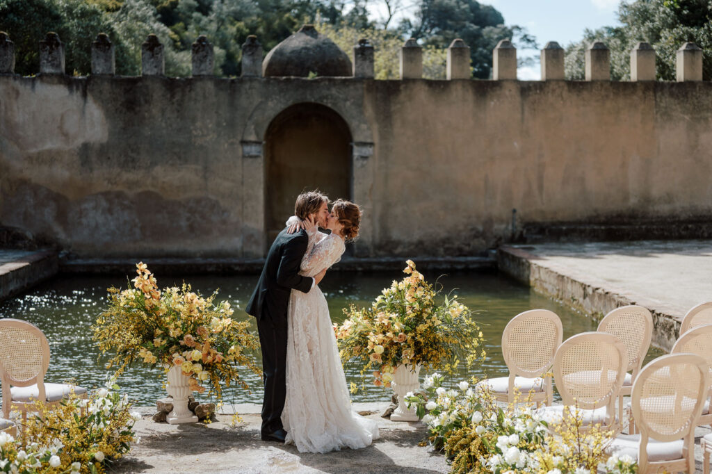 Wedding couple holding each other and kissing at an outdoor venue surrounded by potted flowers