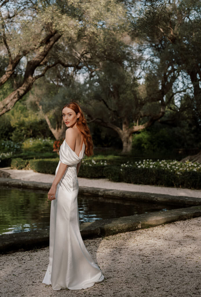 Wedding and Elopement photographer, bride in satin gown posing by reflective pond in garden