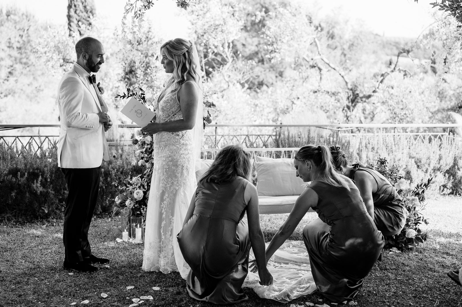 wedding photography bride and groom sharing vows during outdoor ceremony while bridesmaids adjust dress