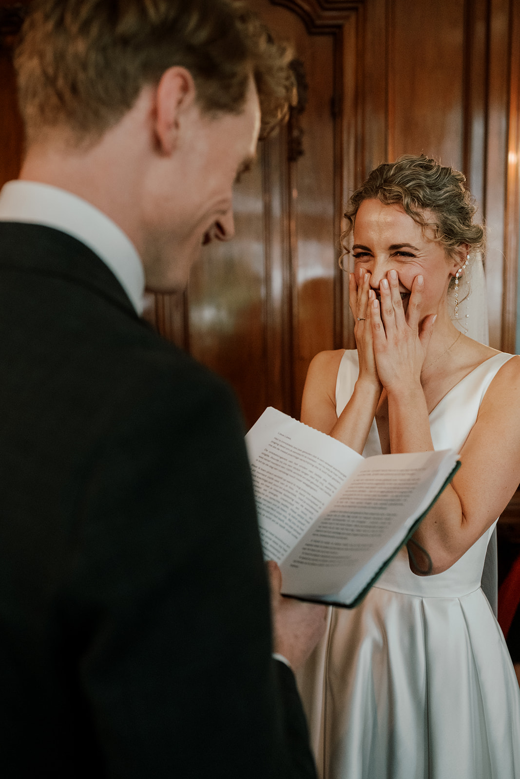 Bride laughing with her hands over her face while the groom reads his vows during the wedding ceremony, wedding photographer Amsterdam 