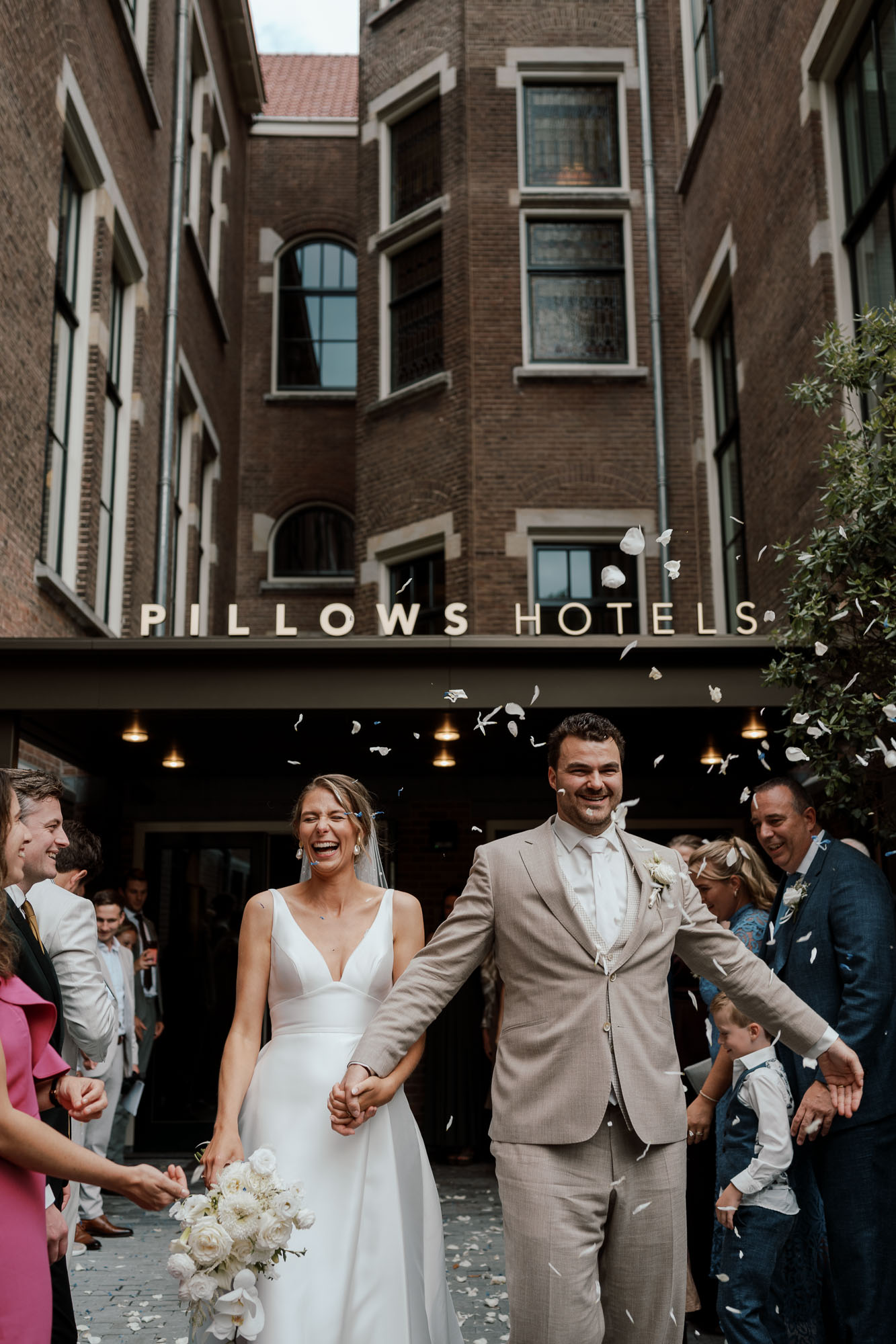 wedding photography, Just married couple walking out of Pillows Hotel holding hands, smiling as guests throw flower petals in celebration